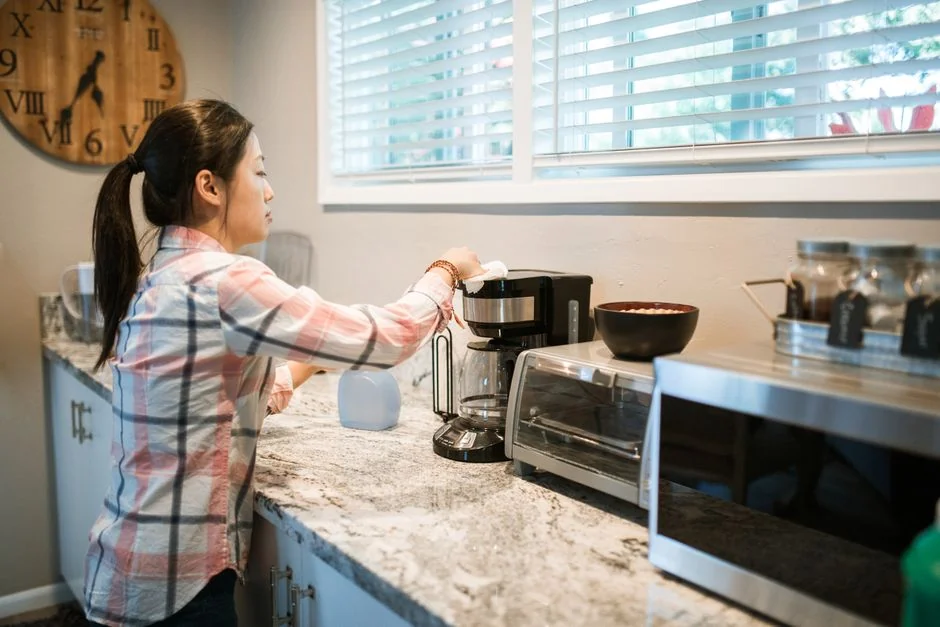 a-woman-in-a-green-shirt-and-black-gloves-vacuuming-a-gray-ottoman-5txz228u4eo